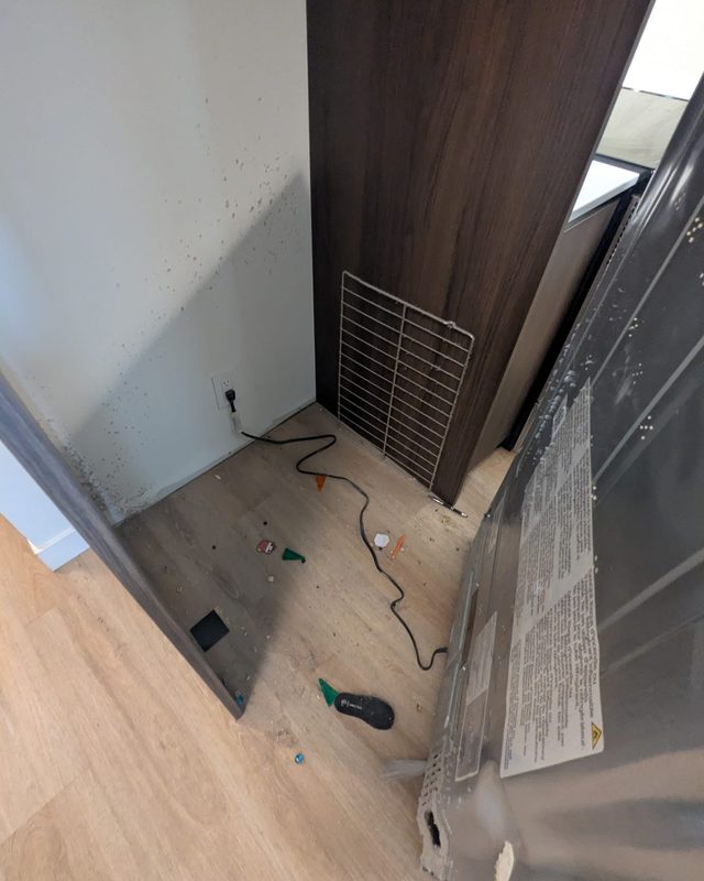 Move-out before: fridge pulled out, floor behind it covered in debris and the wall splattered