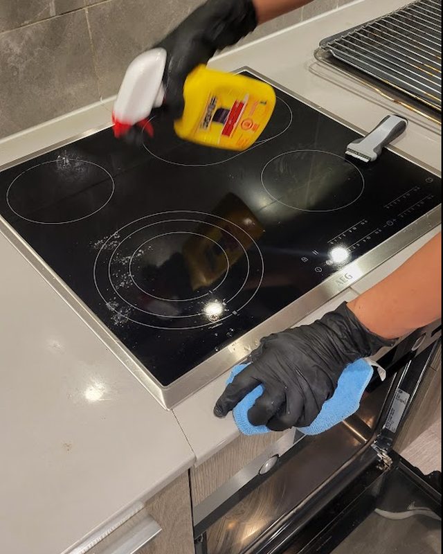 Cleaner spraying and wiping a glass cooktop